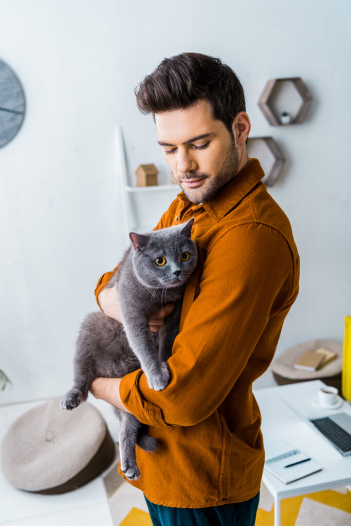 man in yellow shirt standing while holding a gray cat in pet therapy in orange county