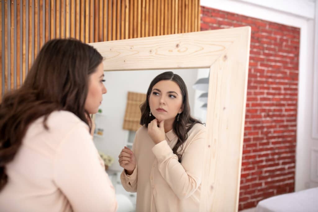 woman struggling with bulimia looking in mirror at reflection - bulimia face and bulimia cheeks