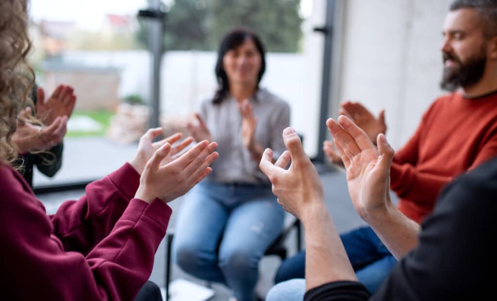 Men and women sitting in circle during group therapy, clapping.